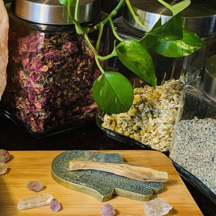 palo santo and hamsa evil eye laying on wooden table with herbs and plants in background