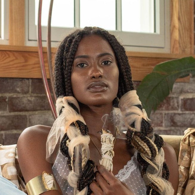 black woman with braids using sage causing smoke looking at peace in a room